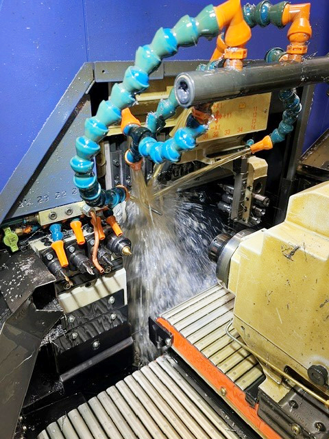 CNC-maskin i drift med kylvätska som flödar kraftigt från ledbara blå och orange flexibla slangmunstycken mot skärområdet, fotograferad uppifrån inuti maskinens kåpa.