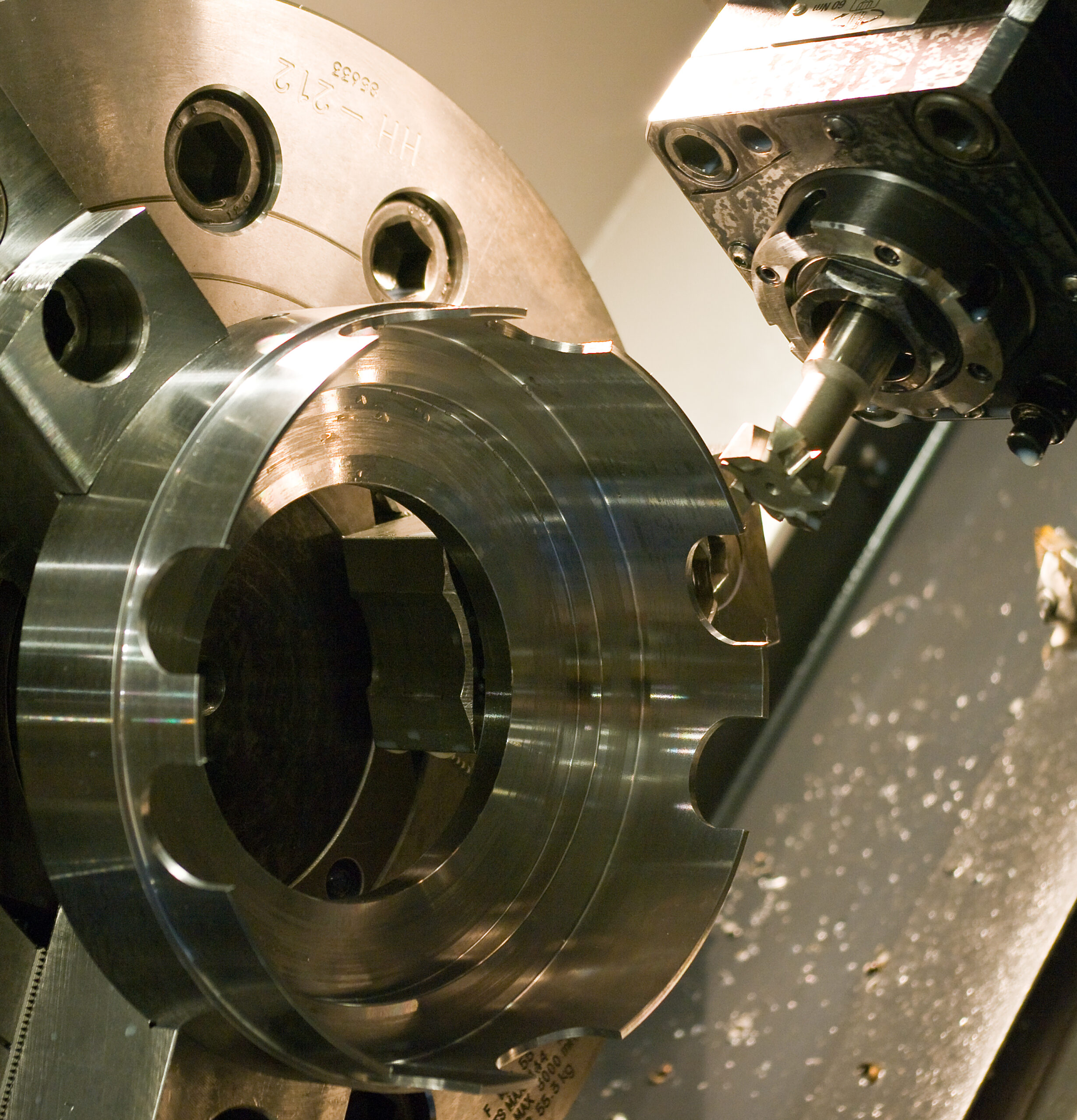 Närbild på ett stort cylindriskt metallämne uppspänt i en CNC-svarvs chuck, under bearbetning med ett svarvstål med hårdmetallskär, med spånor synliga på sängen.